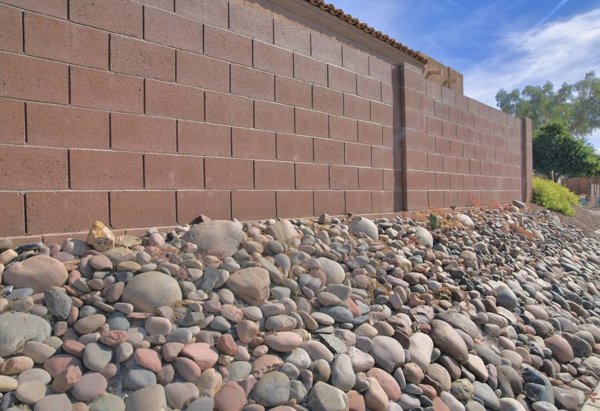 Red-brown block wall at the top of a slope covered in rounded river rock