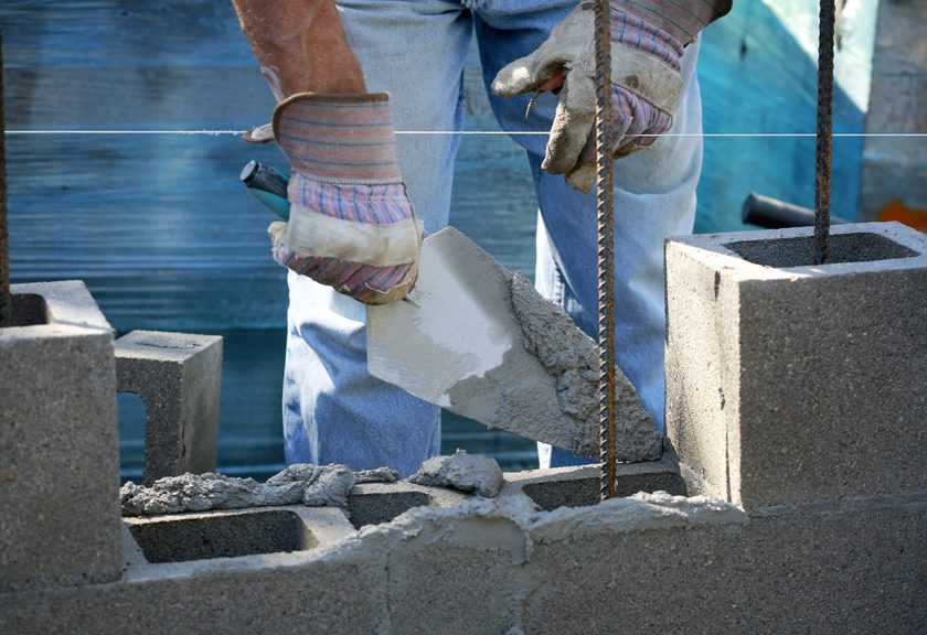 Mason holding a trowel of mortar between block cells and upright steel bars