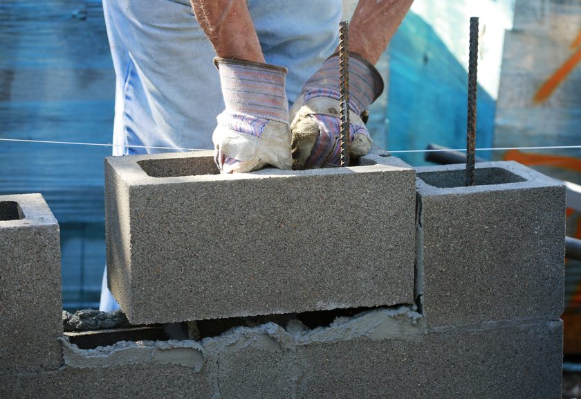 Gloved hands lowering a hollow concrete block over an upright steel bar